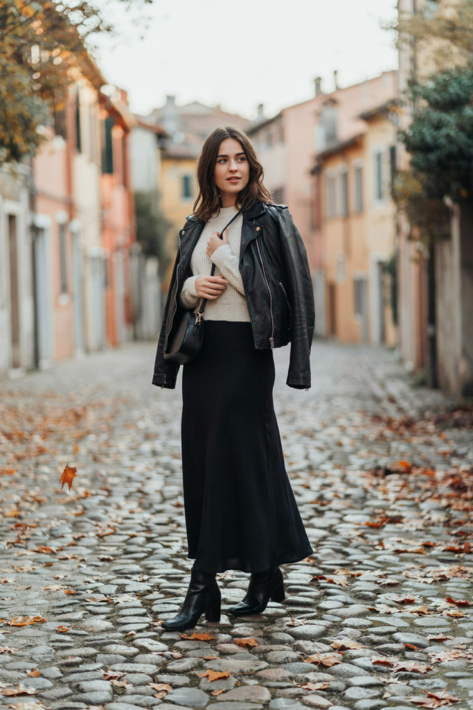 A girl with black ankle-length maxi skirt styled with a simple cream fitted sweater and black leather jacket.