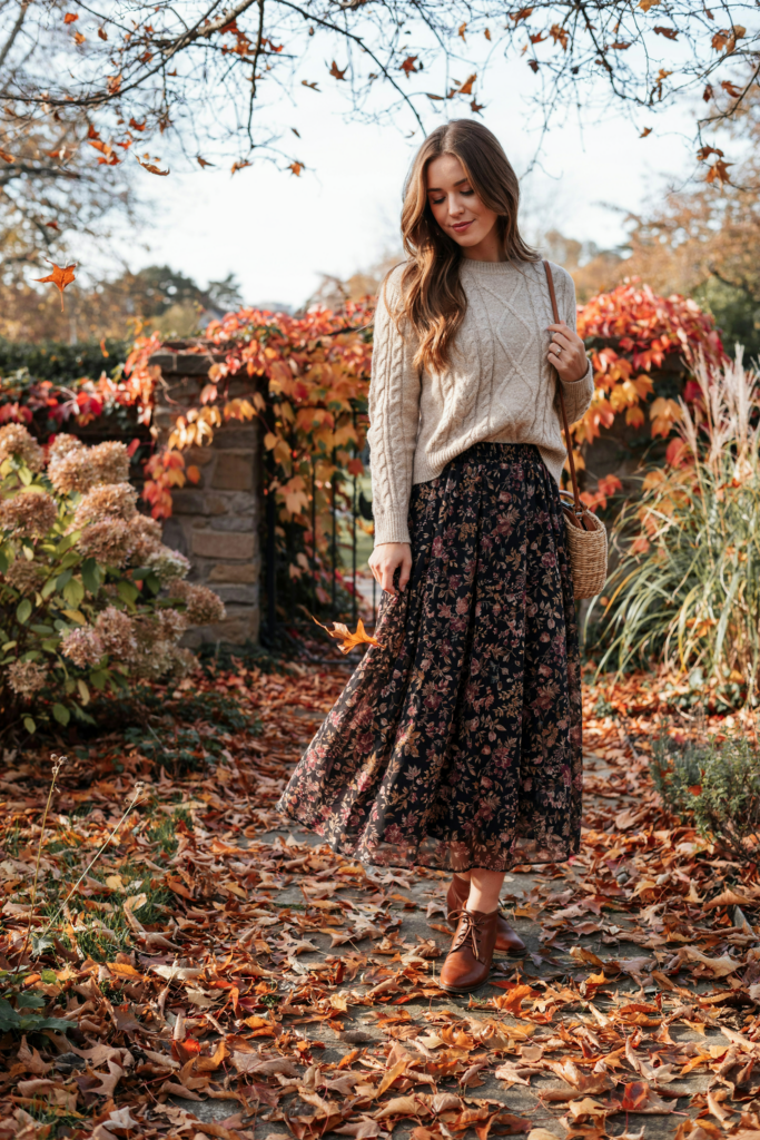 ark floral ankle-length maxi skirt with burgundy and muted brown flowers, cream knit sweater, brown ankle boots, small woven handbag, autumn garden setting with fallen leaves, soft feminine styling, warm natural light.